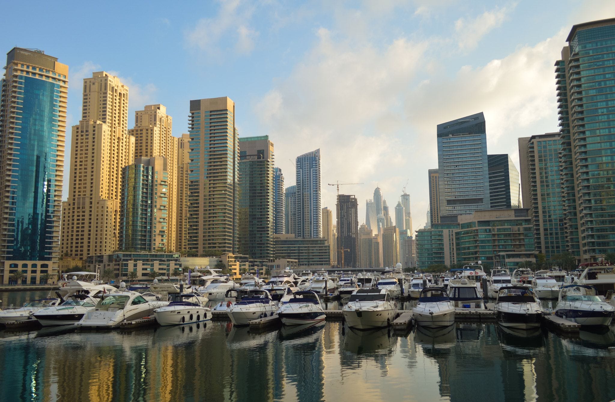 Yachts moored in Dubai Marina with the residential towers behind them in late-afternoon light