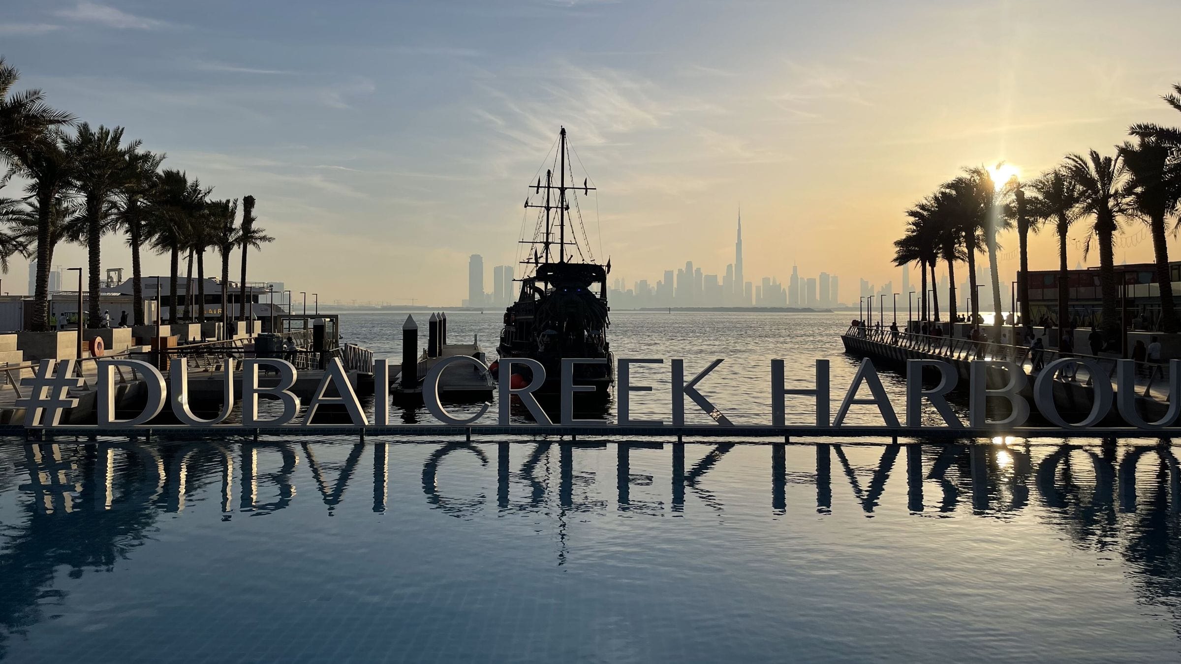 The Dubai Creek Harbour sign on the waterfront with the Downtown skyline behind
